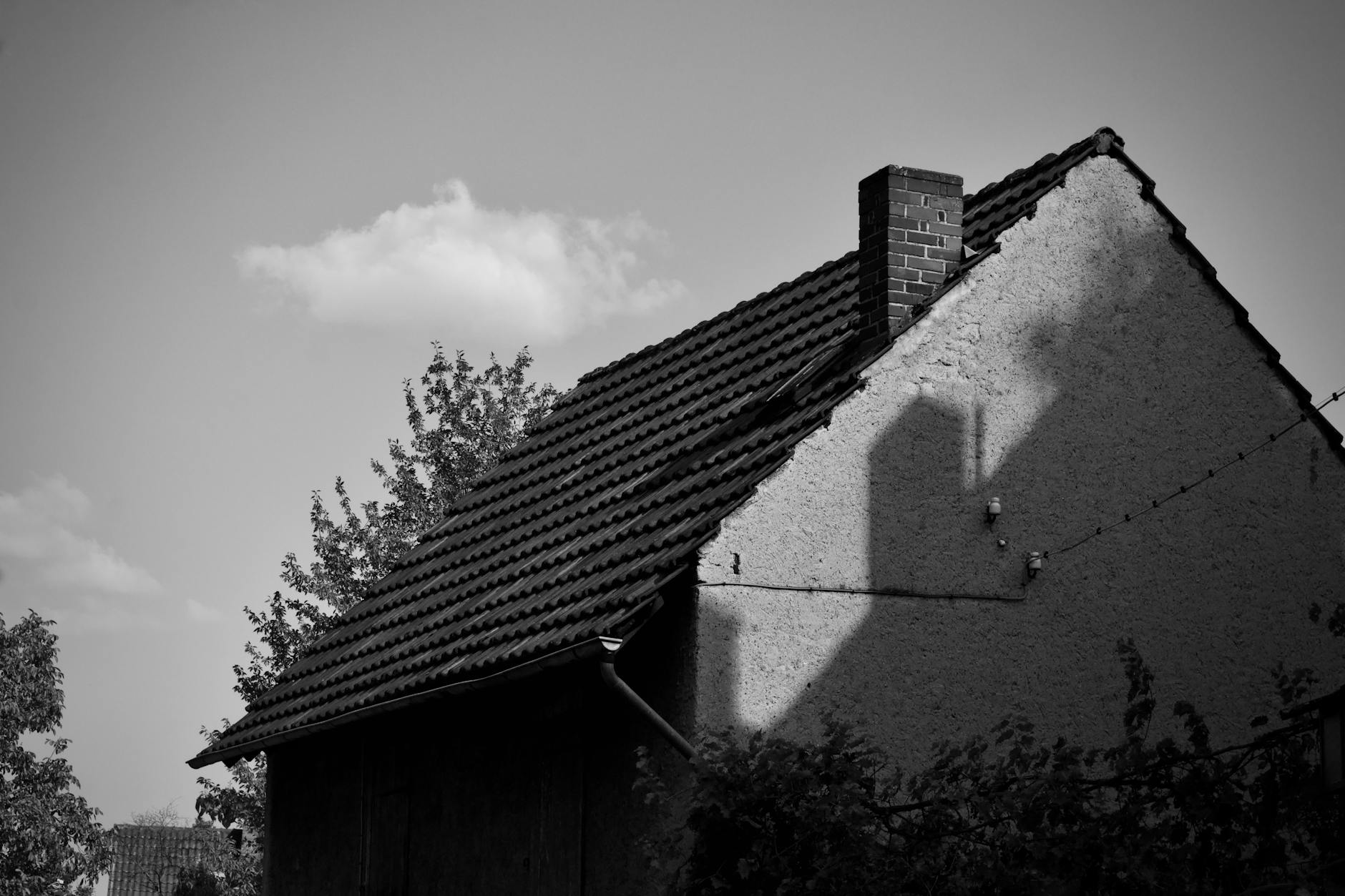 Dom z kominem na tle jasnego nieba, czarno-białe ujęcie