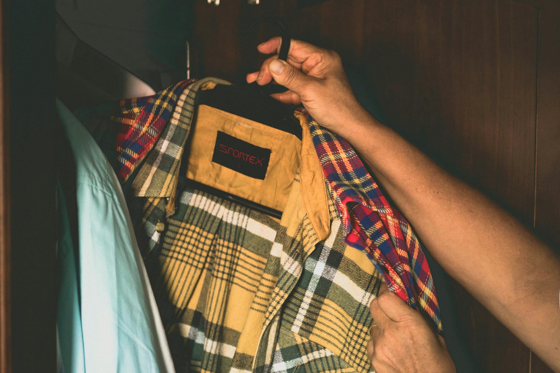 Osoba trzyma w szafie męską koszulę w kratę na wieszaku