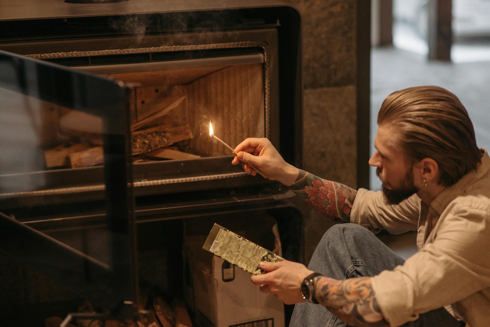 Brodaty mężczyzna rozpala drewniany kominek w salonie