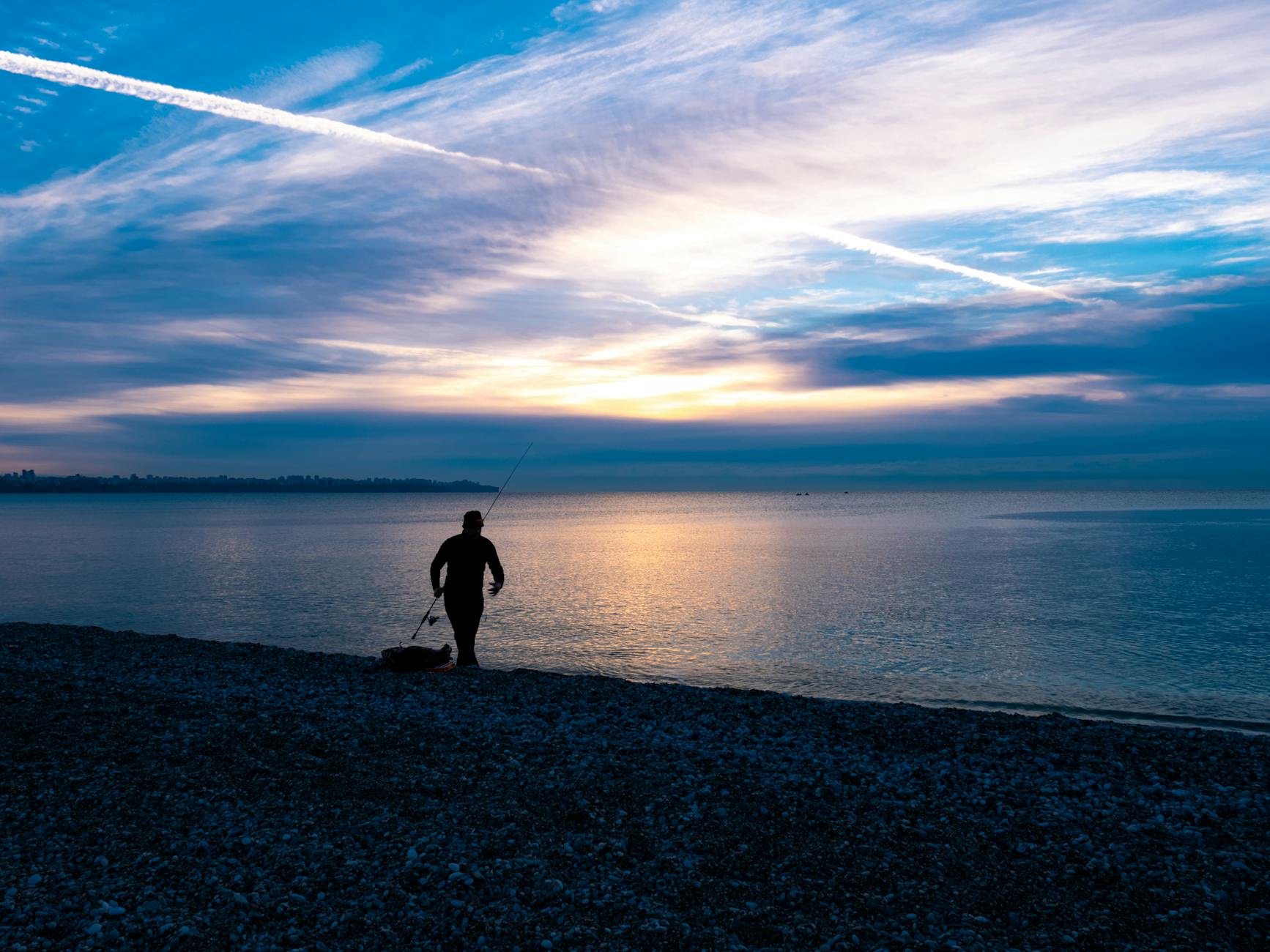 Wędkarz o świcie na spokojnej plaży, sylwetka na tle wschodu słońca