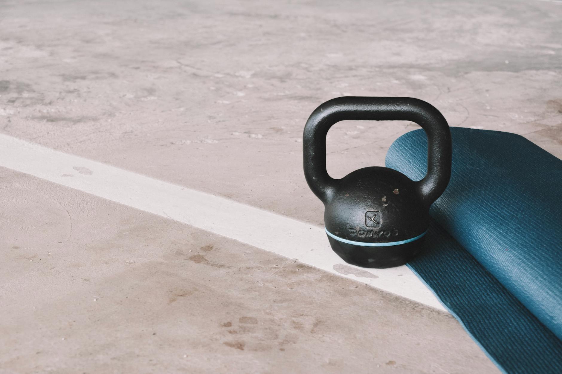 Kettlebell i niebieska mata do ćwiczeń na betonowej podłodze domowej siłowni