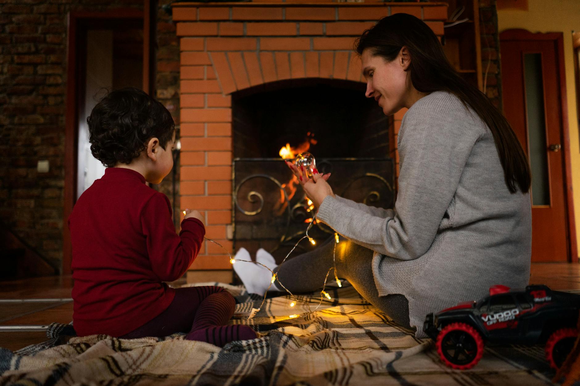 Mama z dzieckiem bawią się światełkami przy kominku w salonie